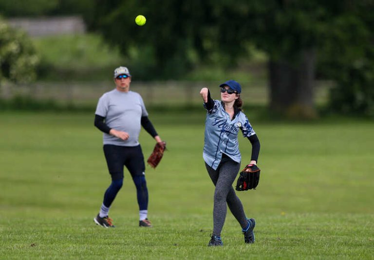 Female player in the foreground releasing a throw, second player visible further back on a grass outfield