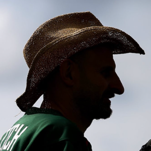 Dramatic silhouette portrait of Dales player Fletch wearing a straw cowboy hat, lit from behind against a bright sky