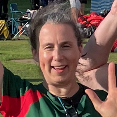 Close portrait of Dales player Jane smiling with arms raised in green and red kit, other players and equipment visible in the background