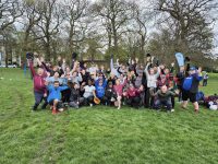 Large group of players in mixed softball kit cheering with arms raised at a Shake and Bake session in a park on an overcast April day in 2024