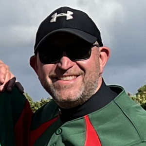 Close portrait of Dales player Steve B in a black Under Armour cap and green kit, smiling on the field