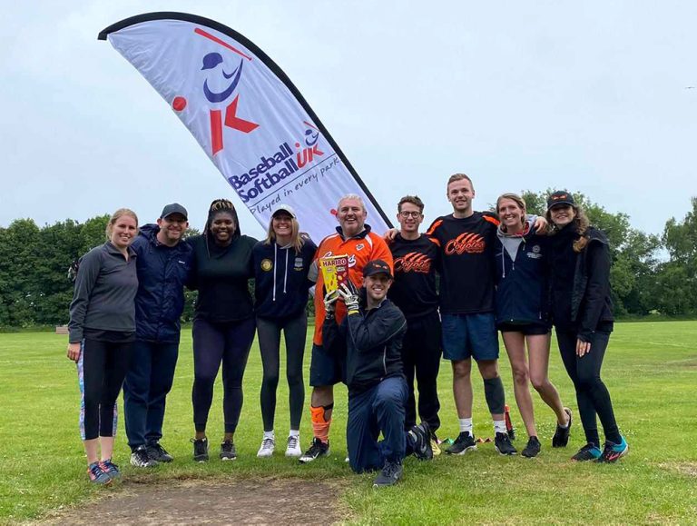 Coyotes players in orange and casual kit posing together beside a Softball England branded banner at an event or registration area