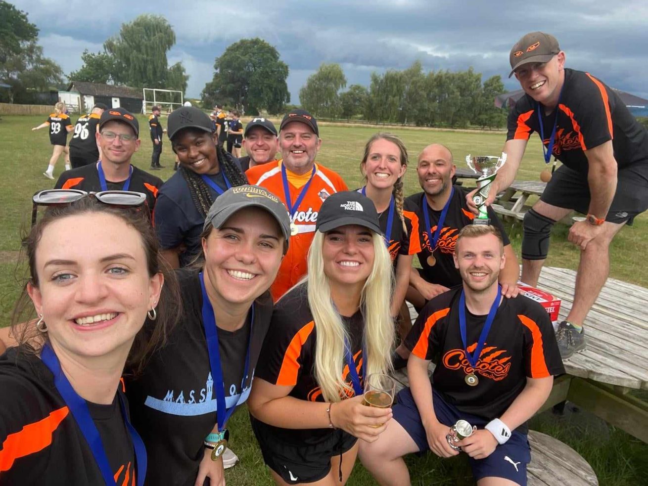 Coyotes players in orange kit taking a group selfie at a fun day or awards event, someone holding a trophy visible in the background