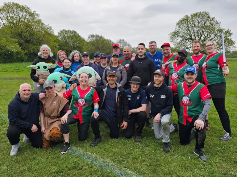 Large group of people posing for photo on grass field, some wearing baseball uniforms and costumes