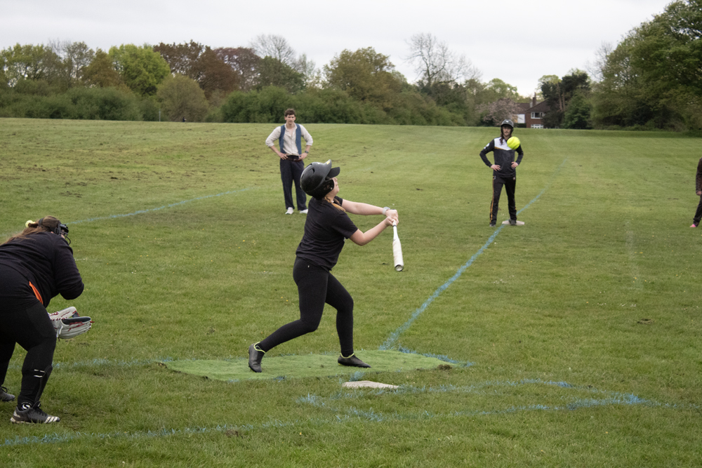 Batting Tee Black Kit Swing Player in black kit taking a clean swing at a batting tee station, batting mat visible beneath them, other players in the background