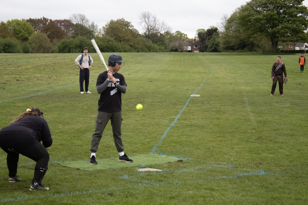 Batting Tee Dark Kit Swing Player in dark kit taking a swing at a batting tee, ball in the hitting zone, open green field around them
