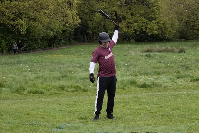 Follow Through Swing Softball player in maroon uniform completing a bat swing follow-through on a grass field