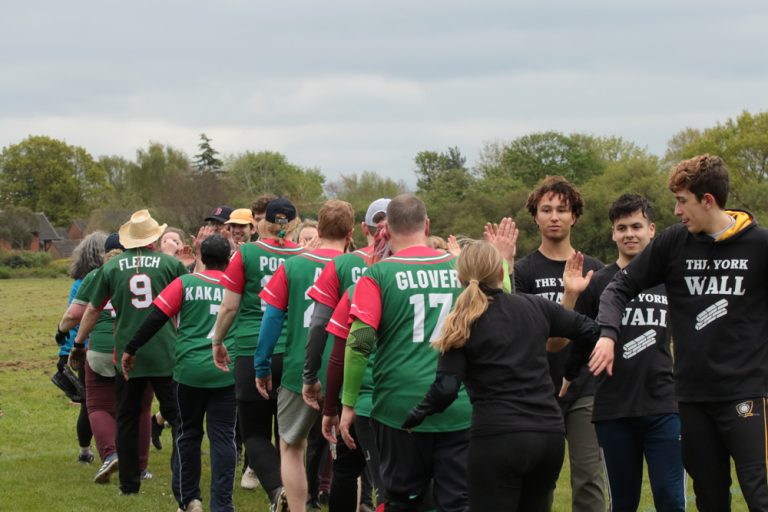 Players from two teams forming a post-match handshake and high-five line on the field, mixed green and black kits