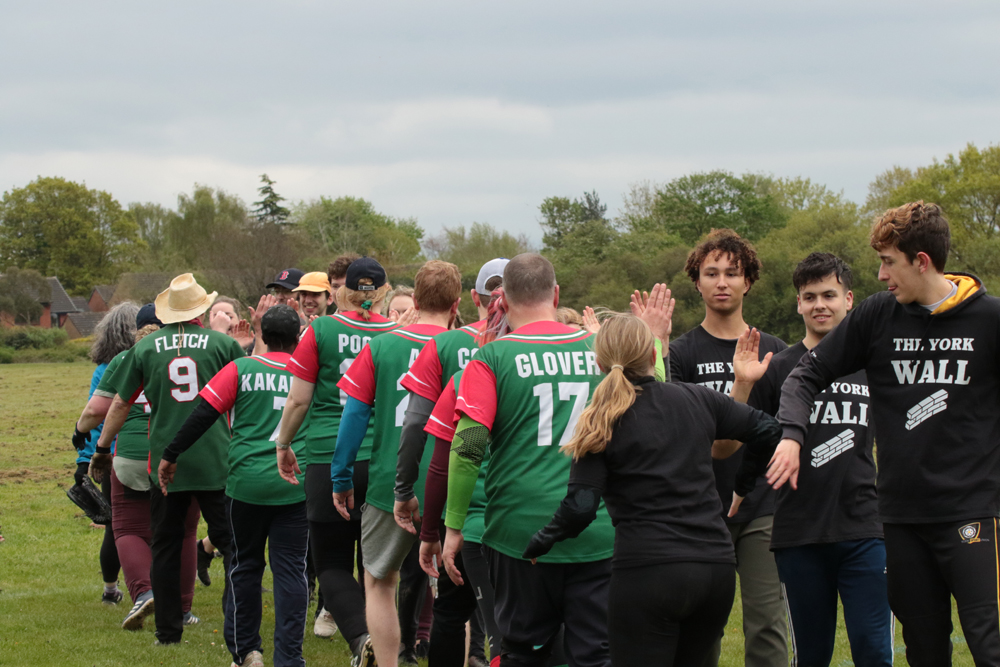 High Fives After Match Players from two teams forming a post-match handshake and high-five line on the field, mixed green and black kits