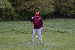 Baseball player in maroon uniform preparing to catch ball in grassy field with trees