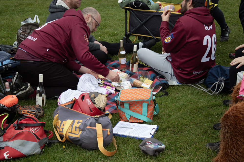 Kit Bags Break Maroon Kit Two players in maroon kit crouched beside kit bags on the grass during a practice break, equipment and snacks visible