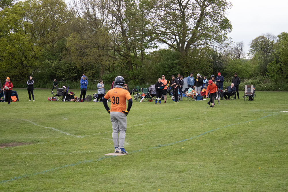 Orange Kit Outfield Watch Player in orange kit number 10 standing in the outfield watching play, dugout area with spectators visible behind them