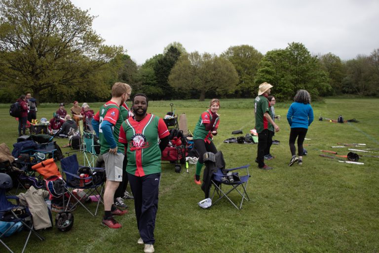 Group of players in mixed red and green kits gathered in the outfield beside kit bags and equipment between drills