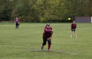 Softball pitcher releasing the ball mid-throw with a yellow ball visible in the air