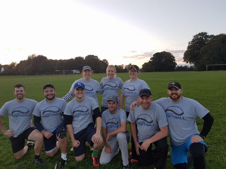 Team in matching grey kits posed for a group photo on a grass field at dusk