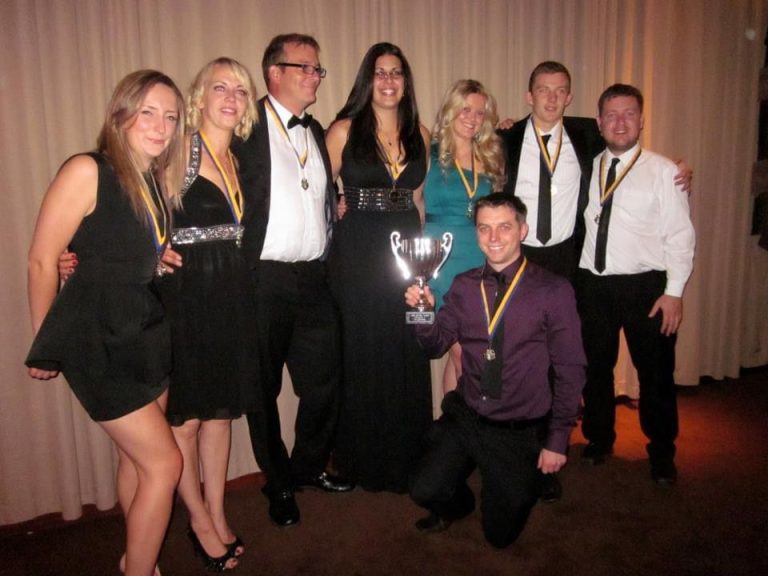 Group photo of Leeds softball players in formal evening wear at an awards dinner, silver trophy cup visible