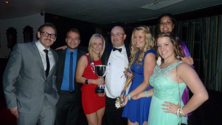 Group photo at a formal softball awards evening, players in smart dress with a silver cup trophy