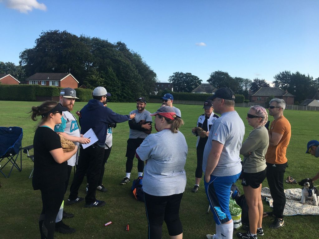 Players gathered in a group on an outdoor grass field for a pre-practice briefing or coaching session