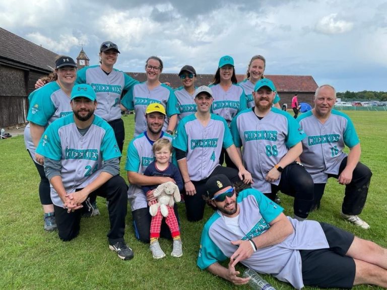 Team group photo in teal and turquoise kits on a grass field, a baby among the group