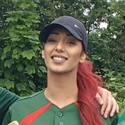 Headshot portrait of Sanz in a green and red Dales kit with red hair, smiling outdoors among green foliage