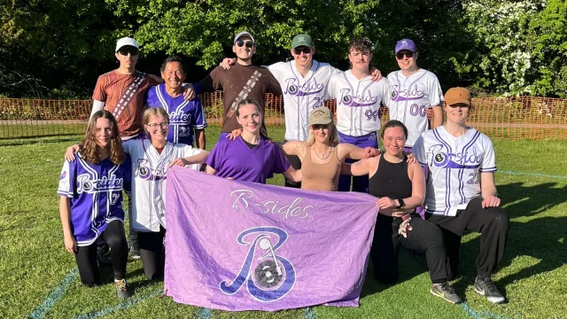 B-Sides team group photo holding a purple B-Sides banner, players in mixed clothing on a grass field
