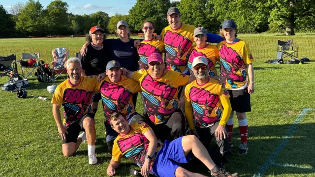 BAM team group photo in colourful multi-colour jerseys with yellow, pink and blue pattern, on a grass field