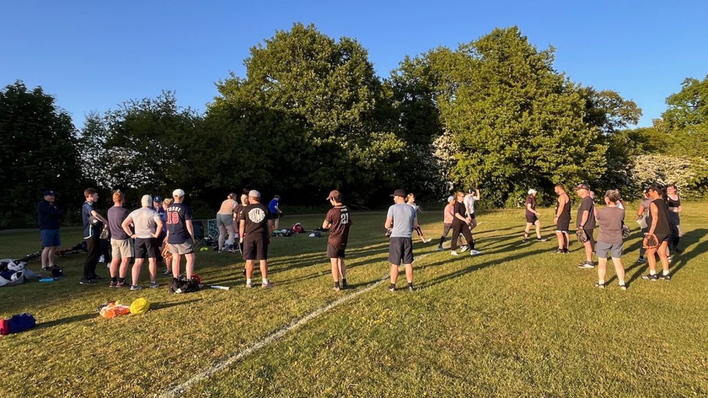 Players spread out across the field during an evening outdoor practice session, long shadows in low summer light