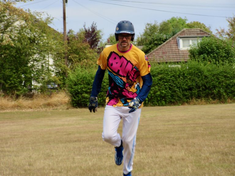 Batter in a brightly patterned jersey and helmet sprinting hard down the line after a hit