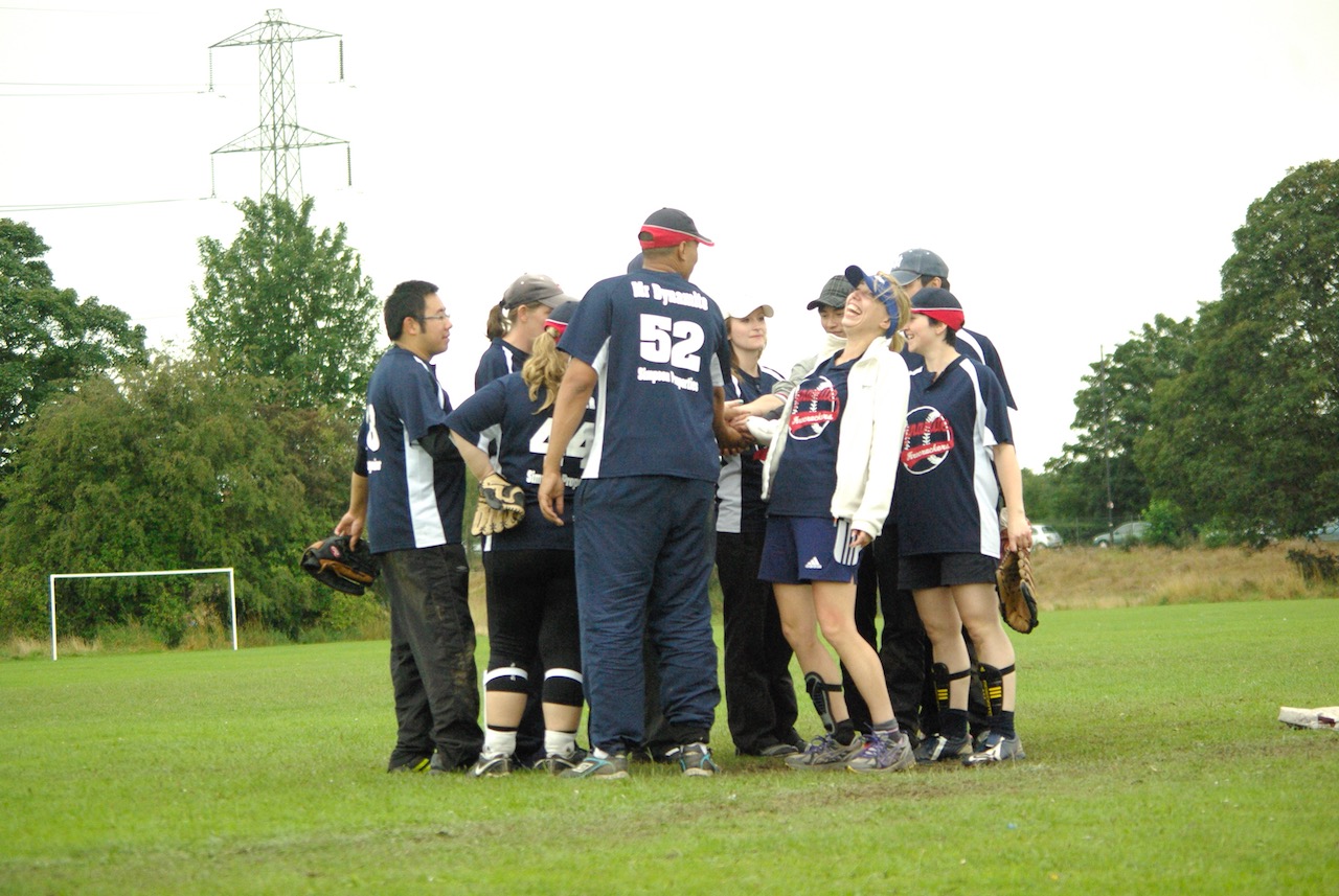 Dynamite softball team in navy kit huddled together on the field, celebrating