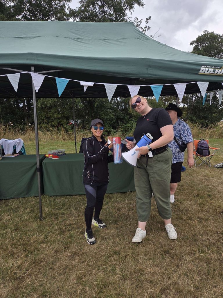 Tournament organiser with a megaphone and clipboard at the gazebo, bunting overhead